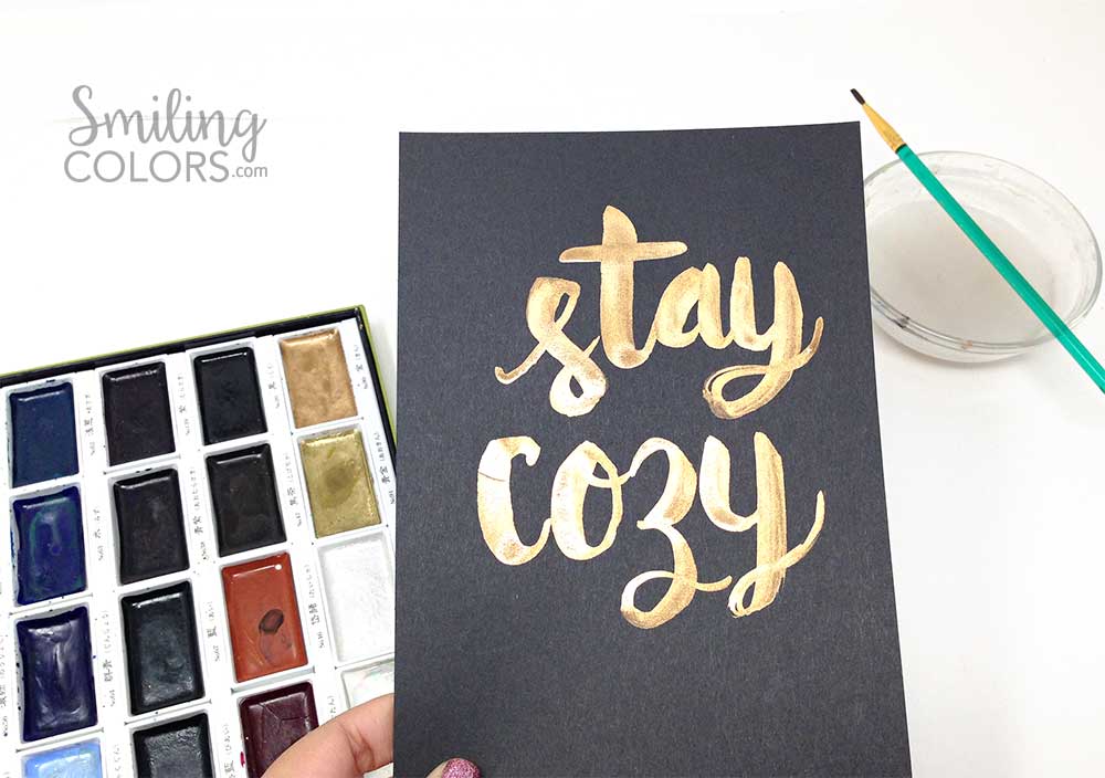 brush lettering on black paper with gold watercolors