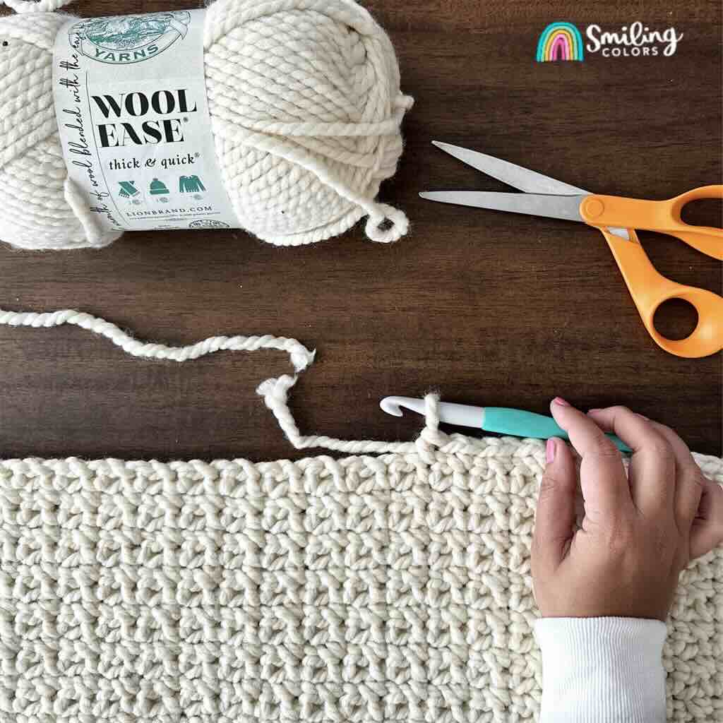 new yarn skein with a scissor next to a blanket in process